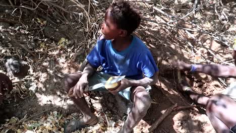 Happy-hadzabe-tribe-boy-peeling-a-Baobab-root-with-knife-while-a-man-tries-to-find-more