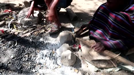 Datoga-tribe-man-blowing-embers-with-a-rudimental-handmade-system-to-melt-metal