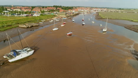 Low-Establishing-Drone-Shot-at-Low-Tide-Down-Wells-Next-The-Sea-Creek-with-Small-Sailing-Boats-and-Dinghies-with-Salt-Marsh-and-Harbour-North-Norfolk-UK-East-Coast