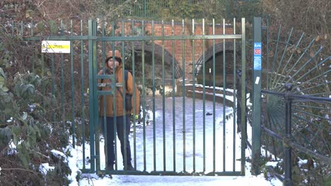 Male-guard-closing-heavy-green-iron-park-gate-to-deny-entrance-to-snowy-winter-pathway