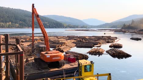 Log-loader-sitting-on-barge-in-water-surrounded-by-floating-logs-at-sawmill