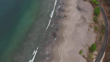 Beach-in-Costa-Rica-with-soft-waves-hitting-rocks-and-creating-round-swirls-near-road,-Aerial-top-view-rotation-shot