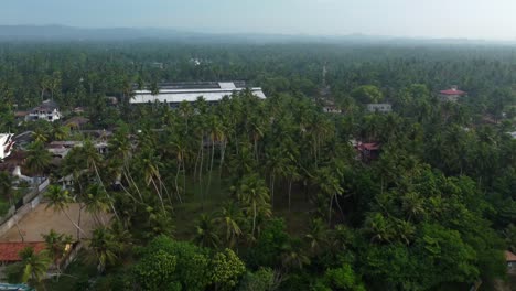 Aerial-pullback-from-countryside-town-surrounded-by-lush-forest-with-morning-haze-in-the-distance,-Sri-Lanka