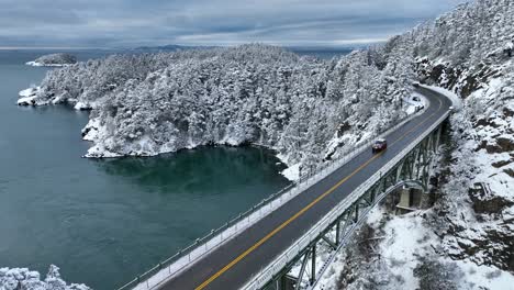Drone-shot-tracking-a-car-driving-across-Deception-Pass-Bridge-in-the-winter-time-with-snow-everywhere