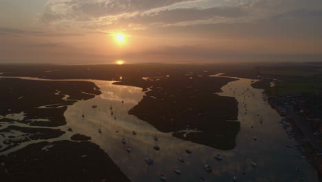 Drone-Shot-Over-Coastal-Town-at-Beautiful-Stunning-Sunrise-at-High-Tide-with-Sailing-Boats-and-Salt-Marsh-and-Creek-in-Wells-Next-The-Sea-North-Norfolk-UK-East-Coast