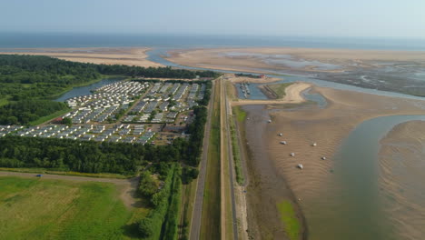 High-Aerial-Drone-Shot-Down-the-Line-of-Wells-Next-The-Sea-Banking-at-Low-Tide-with-Sailing-Boats-and-Static-Caravan-Homes-Park