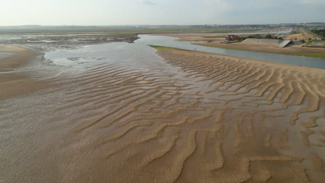 Low-Establishing-Drone-Shot-over-Ripples-of-Sand-at-Low-Tide-in-Wells-Next-The-Sea-Creek-with-Old-Lifeboat-House-North-Norfolk-UK-East-Coast