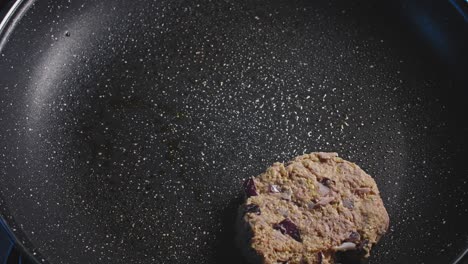 Hand-adding-tuna-fritters-to-an-empty-black-pan-and-gently-pressing-them-to-make-then-flat