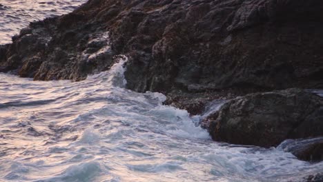 Slow-motion-waves-crashing-on-a-rocky-shoreline-at-sunset,-sunrise,-golden-hour