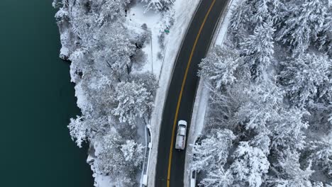 Top-down-shot-of-a-truck-driving-near-a-body-of-water-with-snow-covering-the-land