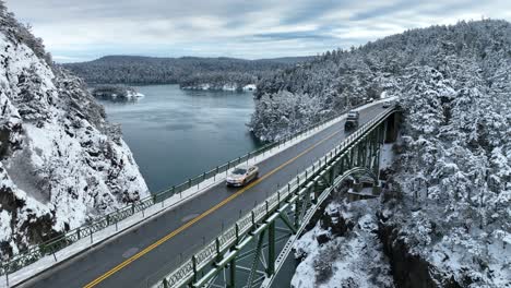 Lowering-aerial-shot-of-cars-passing-over-a-bridge-with-snow-everywhere