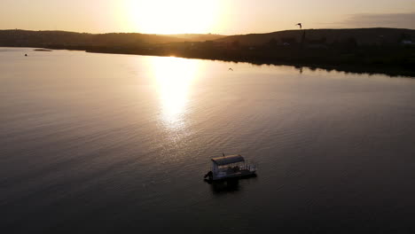 Szenischer-Drohnenrückzug-über-Verankertes-Boot-In-Mündung---Goldene-Sonnenuntergangsreflexion