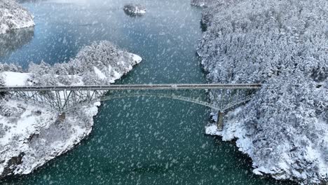 Wide-aerial-view-of-Deception-Pass-bridge-covered-in-snowfall-with-cars-passing-in-between-islands