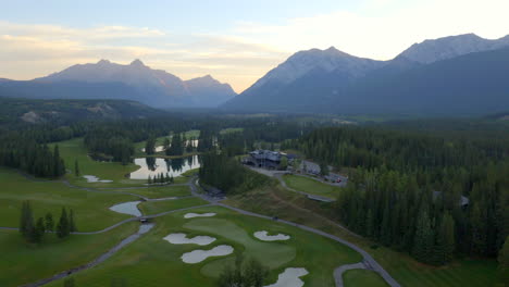 Aerial-view-of-green-golf-course-in-the-rocky-mountains-of-Banff-and-Kananaskis-of-Alberta,-Canada-at-sunrise
