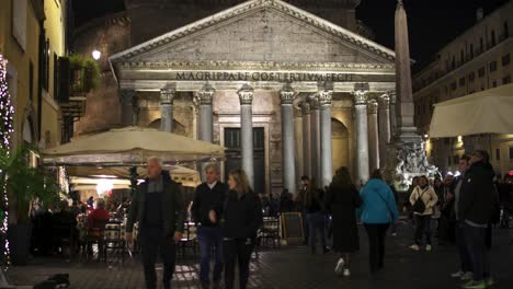 Outdoor-dining-at-a-restaurant-in-Rome,-Italy-at-night-outside-the-Pantheon-with-people-walking