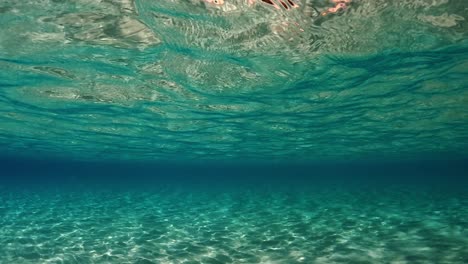 Breathtaking-under-water-scene-of-crystalline-turquoise-tropical-ocean-water-with-rippled-surface-and-reflections-on-seafloor-with-blue-background