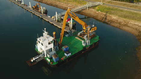 Pullback-Drone-Shot-from-Dredging-Ship-with-Yellow-Crane-Digger-in-Small-Harbour