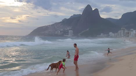 Family-and-dog-playing-on-Copacabana-beach-on-the-weekend,-tide-rolling-in-shore