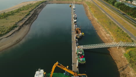 Drone-Shot-of-Digger-with-Crane-on-Boat-and-other-Boats-at-Small-Dock-in-Wells-Next-The-Sea-North-Norfolk-UK-East-Coast