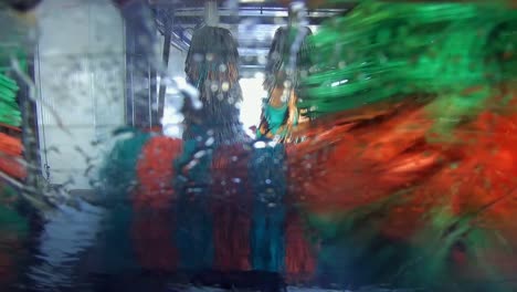 Automatic-car-wash-as-seen-from-back-of-vehicle-moving-through-machine-colorful-rollers-spalshing-water-on-rear-window