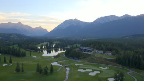 Drone-aerial-view-of-green-golf-course-in-the-rocky-mountains-of-Banff-and-Kananaskis-of-Alberta,-Canada-at-sunrise