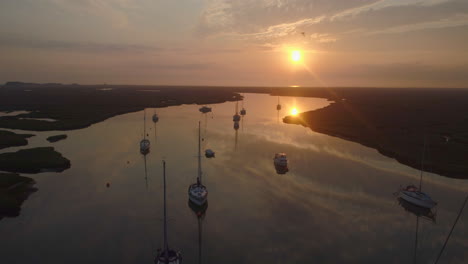 Low-Cinematic-Drone-Shot-of-Sailing-Boats-on-Creek-at-High-Tide-with-Birds-Flying-Past-with-Reflections-at-Stunning-Orange-Sunrise-in-Wells-Next-The-Sea-North-Norfolk-UK-East-Coast