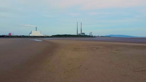 Ein-Niedriges-Drohnenvideo-Des-Leeren-Strandes-Von-Sandymount-Strand-Mit-Der-Müllverbrennungsanlage-Von-Dublin-City-Und-Den-Schornsteinen-Von-Poolbeg