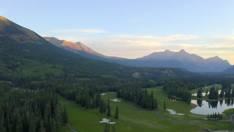 Drone-aerial-view-of-green-golf-course-in-the-rocky-mountains-of-Banff-and-Kananaskis-of-Alberta,-Canada-at-sunrise-in-the-morning