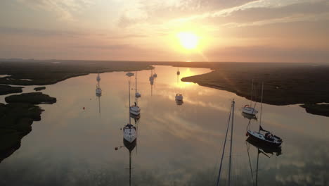 Niedrige-Drohnenaufnahme-Eines-Wunderschönen-Sonnenaufgangs-über-Stillem-Wasser-Mit-Reflexionen-Und-Segelbooten-Und-Salzwiesen-Und-Bach-In-Wells-next-the-Sea-North-Norfolk-UK-East-Coast