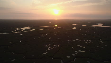 Cinematic-Establishing-Drone-Shot-Over-Salt-Marsh-at-High-Tide-with-Reflections-at-Stunning-Orange-Sunrise-with-Bird-Flying-Through-in-North-Norfolk-UK-East-Coast
