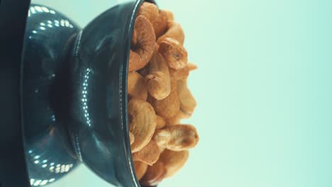 A-vertical-close-up-shot-of-a-roasted-salty-cashew-in-a-black-shiny-bawl-on-a-rotating-stand,-slow-motion,-4k
