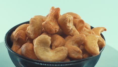 A-close-up-shot-of-a-roasted-salty-cashews-in-a-black-shiny-bawl-on-a-rotating-stand,-slow-motion,-4k,-man-hand-taking-a-cashew-of-the-bawl