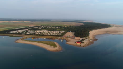Establishing-Drone-Shot-Flying-Over-Sea-at-High-Tide-with-Creek-and-Lifeboat-House-and-Static-Caravan-Park-in-Wells-Next-The-Sea-North-Norfolk-UK-East-Coast