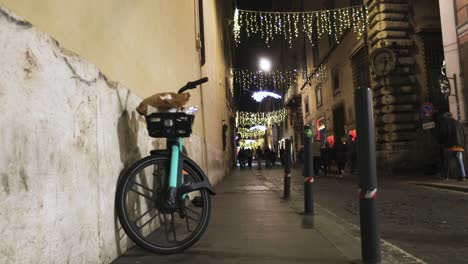 Street-in-Rome,-Italy-at-night-with-bicycle-and-pedestrians-with-an-establishing-shot