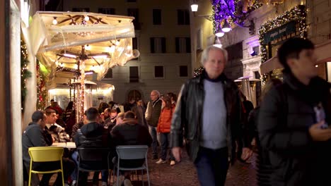 Restaurant-on-a-side-street-in-Rome,-Italy-at-night-with-people-walking-by