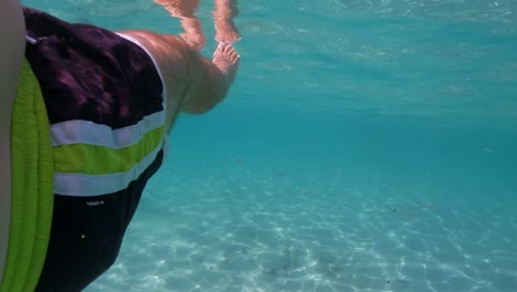 Underwater-personal-perspective-view-of-man-legs-floating-in-clear-transparent-sea-water-beneath-surface,-slow-motion