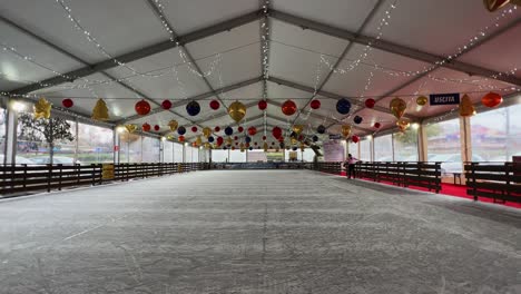 Little-girl-skating-on-ice-alone-in-empty-indoor-ice-rink-with-Christmas-decoration-balls-hanging-on-ceiling