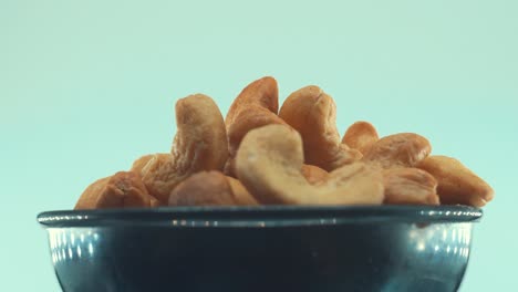 A-close-up-shot-of-a-roasted-salty-cashew-in-a-black-shiny-bawl-on-a-rotating-stand,-slow-motion,-4k