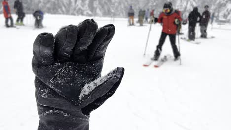Black-winter-glove-covered-in-snow-during-a-snowfall-with-many-skiers-in-the-background