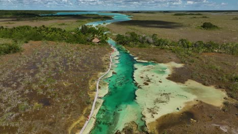 Aerial-view-over-people-swimming-in-the-Bacalar-rapids,-in-sunny-Mexico---reverse,-tilt,-drone-shot