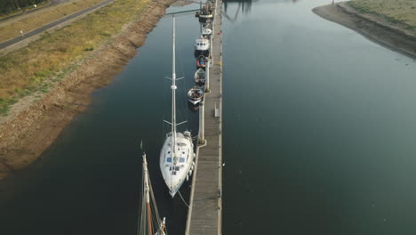 Down-The-Line-Drone-Shot-Along-Small-Pier-with-Sailing-Boats-and-Leisure-Boats-in-North-Norfolk