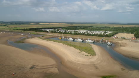 Rotating-Drone-Shot-of-Beach-at-Low-Tide-with-Windmill-Maintenance-Boats-in-Small-Harbour-in-Wells-Next-The-Sea-North-Norfolk-UK-East-Coast