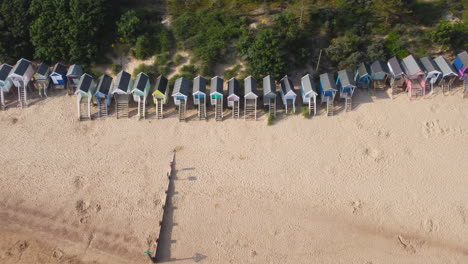 Slider-Drone-Shot-of-Beach-Huts-on-Sandy-Beach-with-Dog-Running-with-Woodland-Behind-in-Wells-next-The-Sea-North-Norfolk-UK-East-Coast