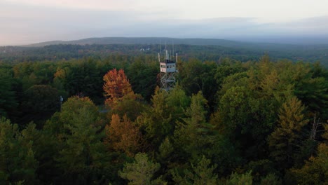 Aerial-drone-of-fire-tower-above-autumn-trees-and-orange-fall-leaves-at-sunrise