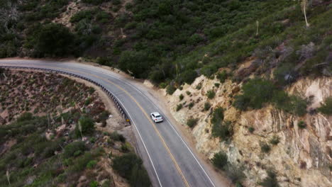 Following-a-white-vehicle-along-a-winding-mountain-two-lane-road---aerial-view