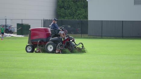Landscaping-worker-mows-a-grass-soccer-field-with-a-lawnmower-in-the-summer-during-the-day