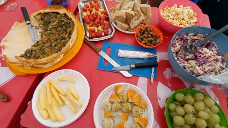 Picnic-table-full-of-food,-pizza,-cheese,-fruit,-olives,-bread-and-tomatoes