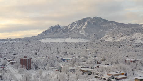 High-drone-shot-moving-right-of-Boulder-Colorado-and-rocky-Flatiron-mountains-after-large-winter-snow-storm-covers-trees,-homes,-streets,-and-neighborhood-in-fresh-white-snow-for-the-holidays