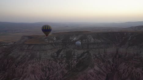 Aerial-view-of-a-blue-and-yellow-balloon-flying-over-the-red-valley-of-Cappadocia