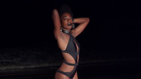 Zoom-in-close-up-of-a-young-African-woman-standing-on-the-beach-at-night-in-a-bikini